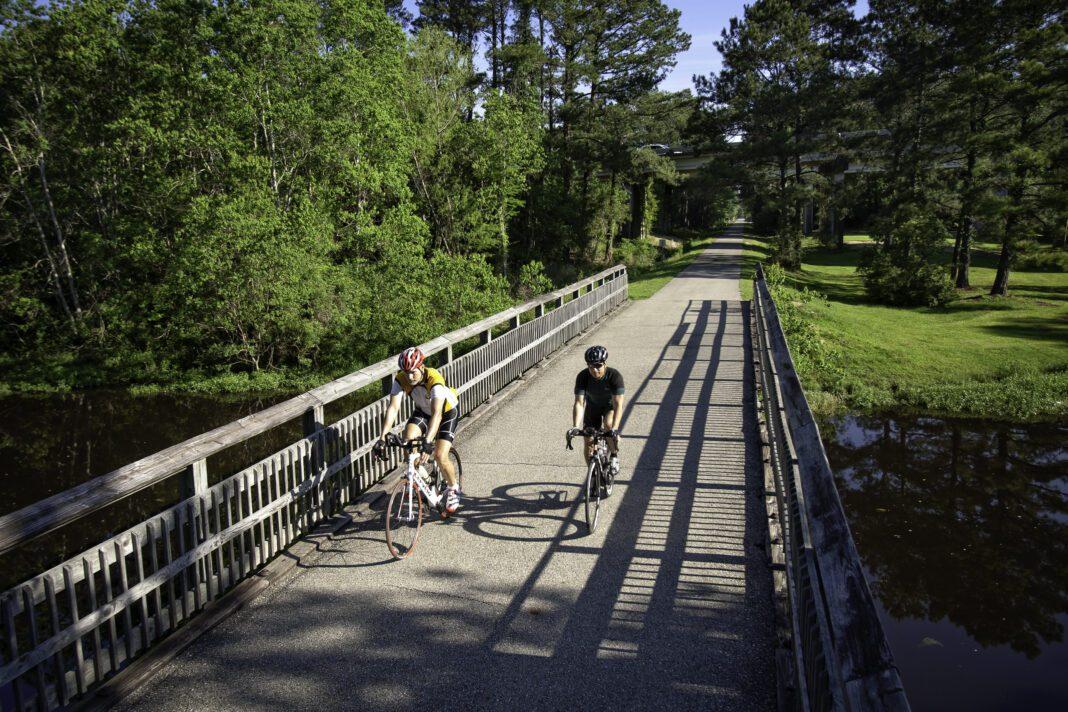 E-bike rentals at Brooks Bike Shop on the St. Tammany Trace — two riders crossing a wooden bridge on the rail trail